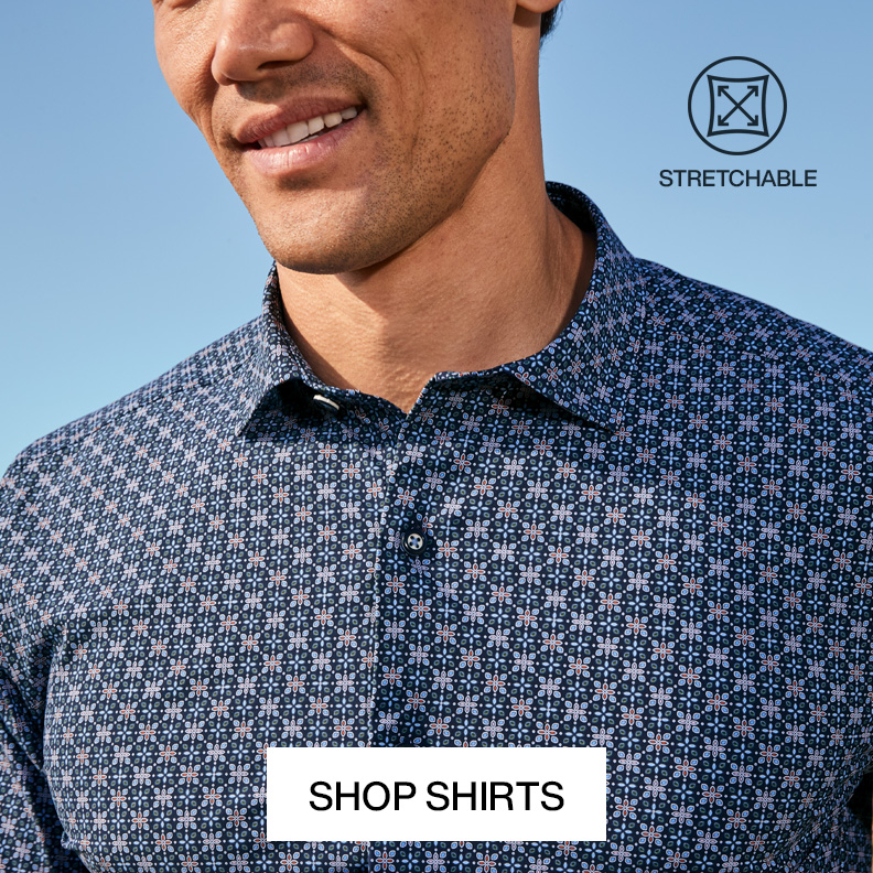 A man is pictured outside with tropical greenery surrounding him. He is wearing a gray plaid blazer, a light blue button-down shirt, and white pants with a Shop Blazers button at the bottom of the image.