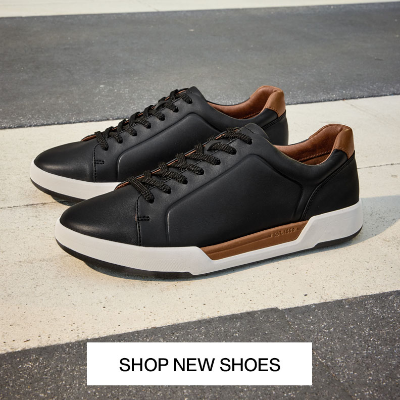 Pair of black leather men's sneakers with white soles and brown accents on pavement with text that reads shop new shoes.