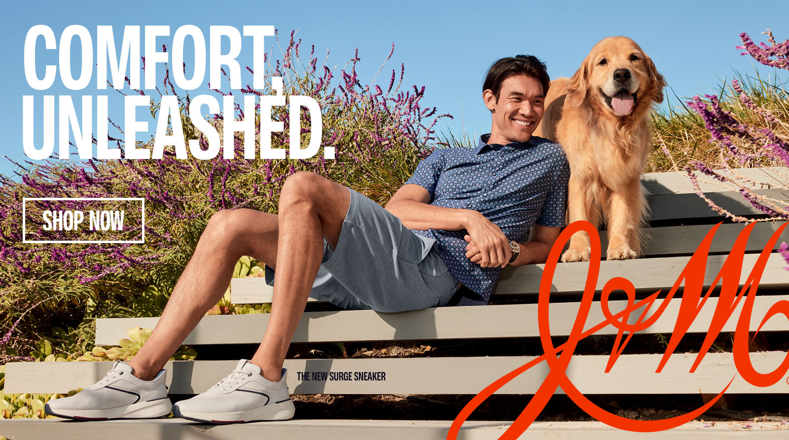 Man dressed in a blue polo and blue shorts with sneakers on leaning on steps with a Golden Retriever standing on the steps above him.