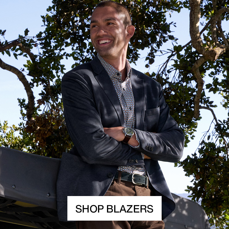 Man leaning against car with crossed arms wearing a blazer, patterned button-up and khakis.