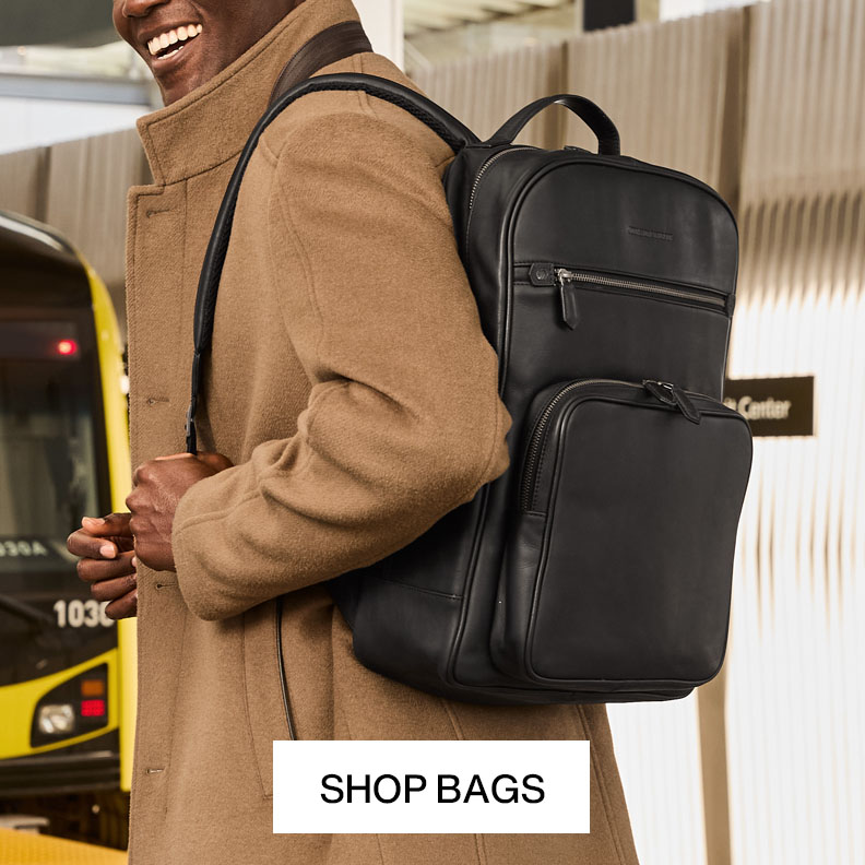 Man wearing a tan jacket and carrying a black leather backpack while traveling with text that reads shop bags.